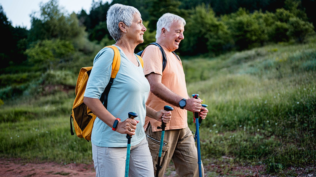 Older couple hiking outdoors with walking poles on a scenic nature trail.