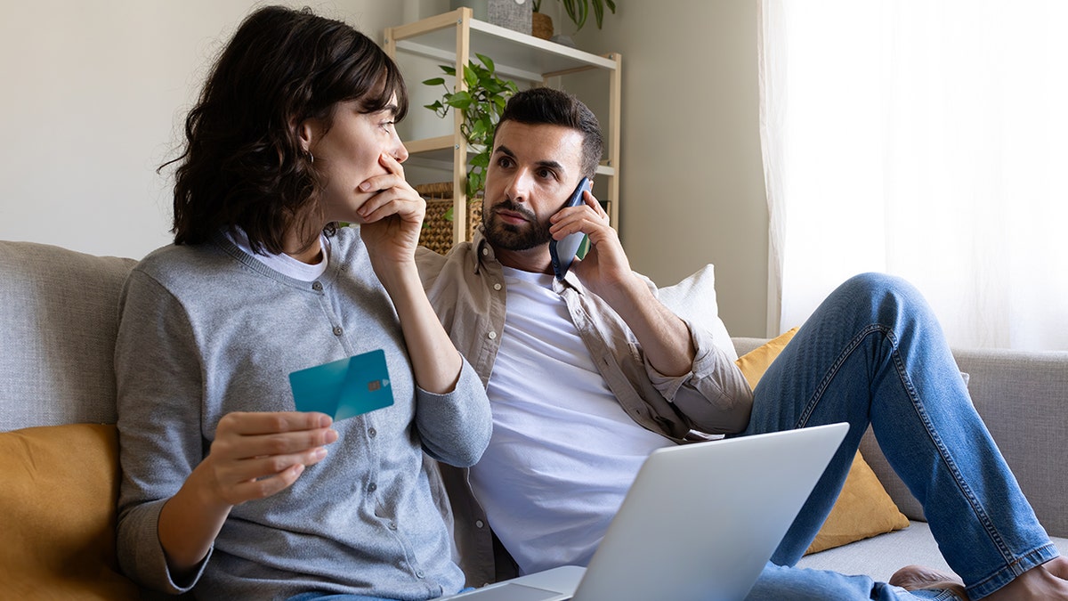 A couple looks worried at a credit card while on the phone.
