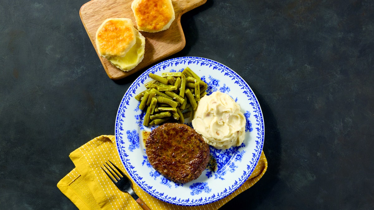 Cracker Barrel's Hamburger Steak is shown on a plate with a side of green beans, mashed potatoes and two biscuits.