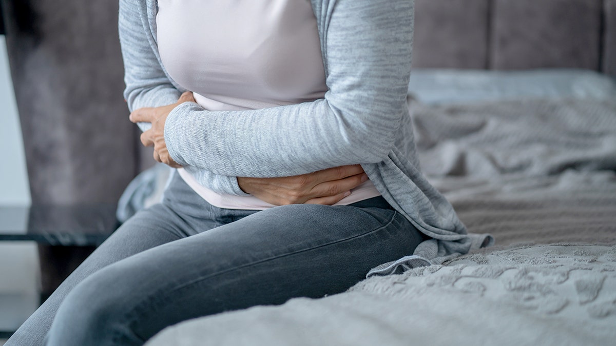 Woman holding her tummy and sitting connected a furniture appearing to acquisition abdominal pain.