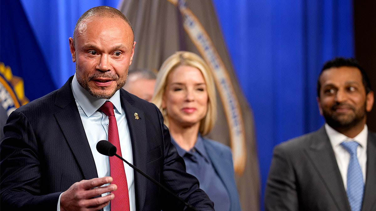 Dan Bongino speaks at a podium while standing with Pam Bondi and Kash Patel during a news conference.