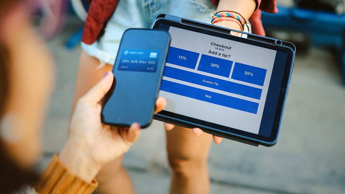 Woman uses her smart phone to pay contactless in a cafe in Santa Monica, California. The waitress is also using a digital tablet for the checkout as well as tipping.