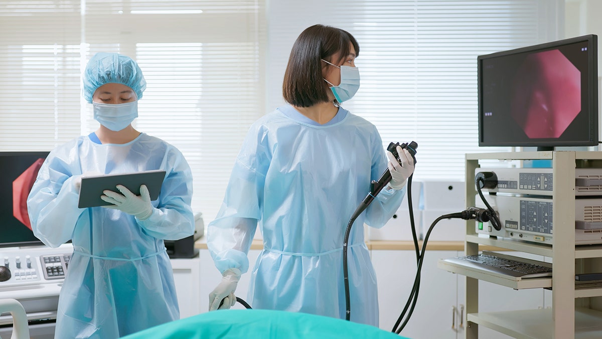 ক্লিনিকাল সেটিংয়ে গ্যাস্ট্রোইনটেস্টাইনাল প্রক্রিয়া চলাকালীন প্রতিরক্ষামূলক গিয়ারে মেডিকেল কর্মীরা এন্ডোস্কোপি সরঞ্জাম প্রস্তুত করছেন।