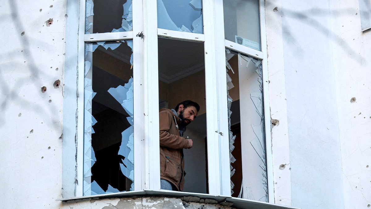Man peers out from a shattered apartment window after an overnight aerial attack damaged his building.