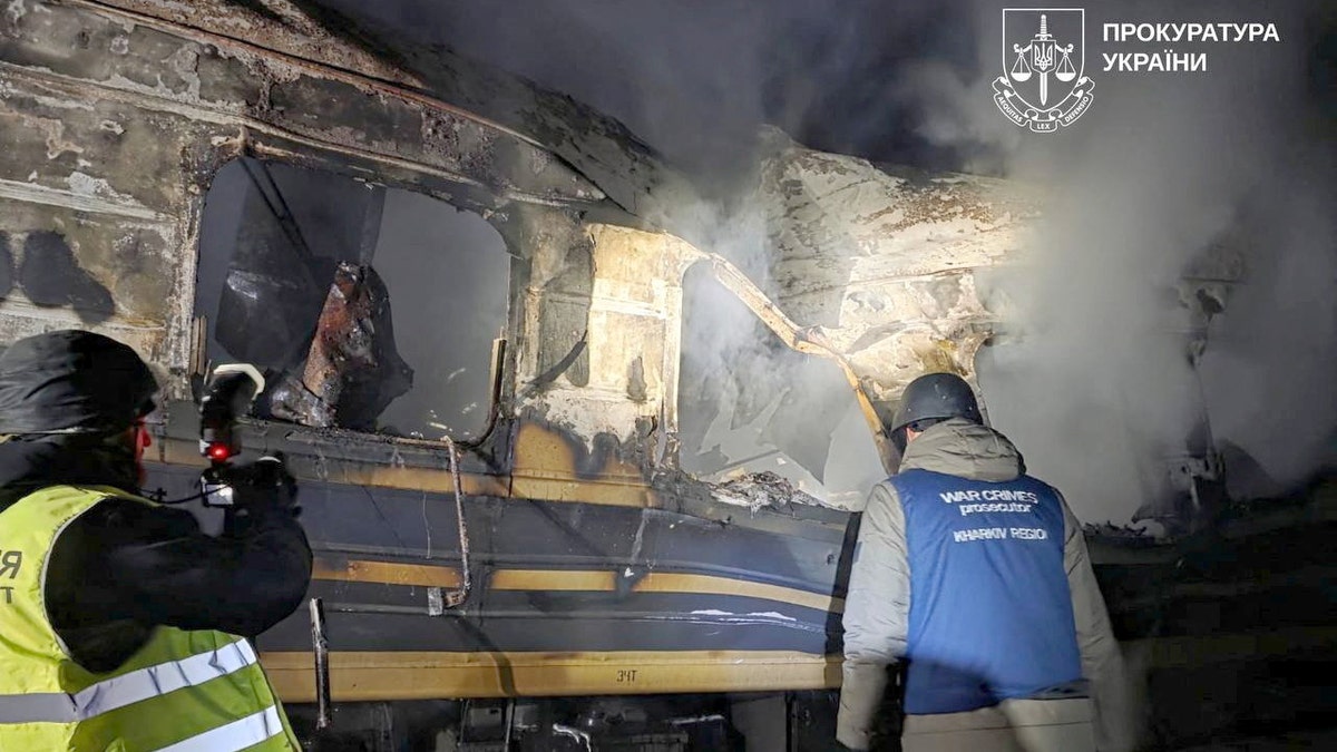 Officials conduct an on-site investigation beside a damaged passenger train following an aerial attack.