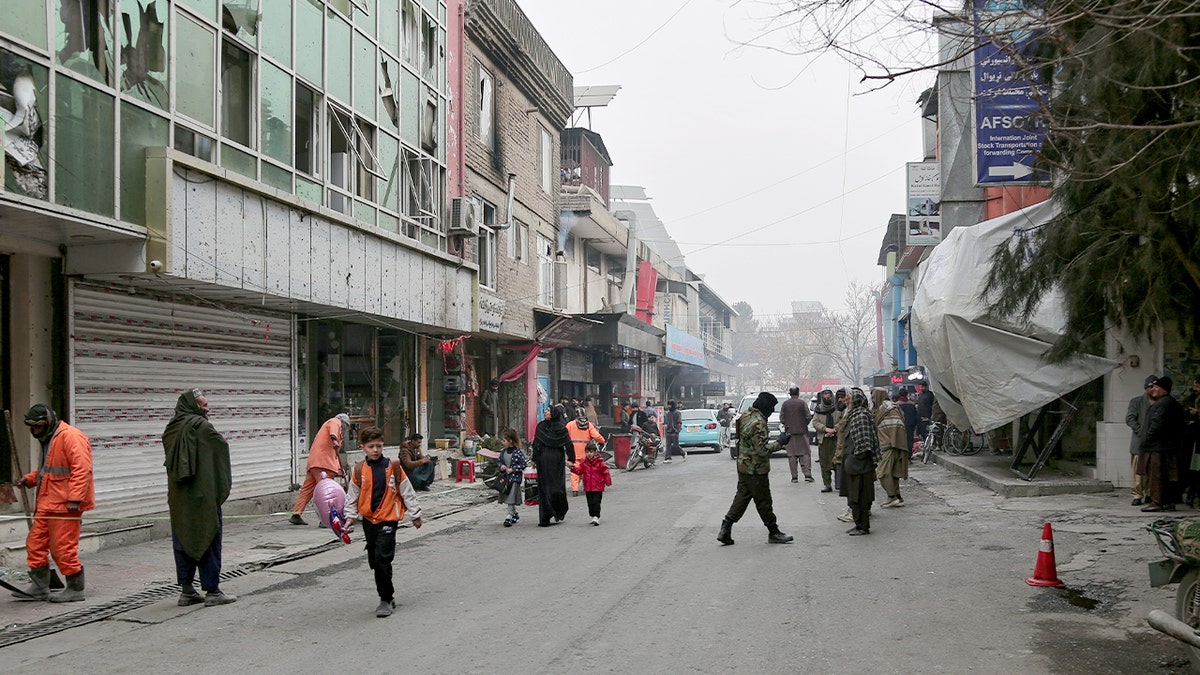 Cleanup crews work amid damaged surroundings while armed security personnel stand guard outside a restaurant entrance following a deadly blast.