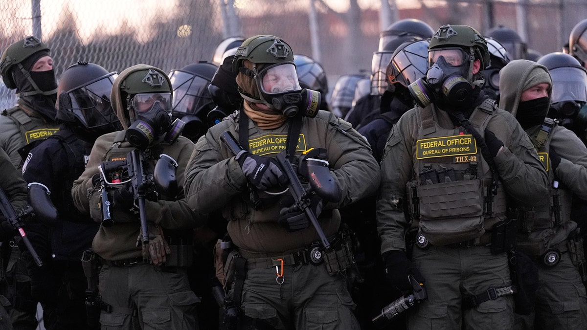Federal officers hold weapons and wear gas masks