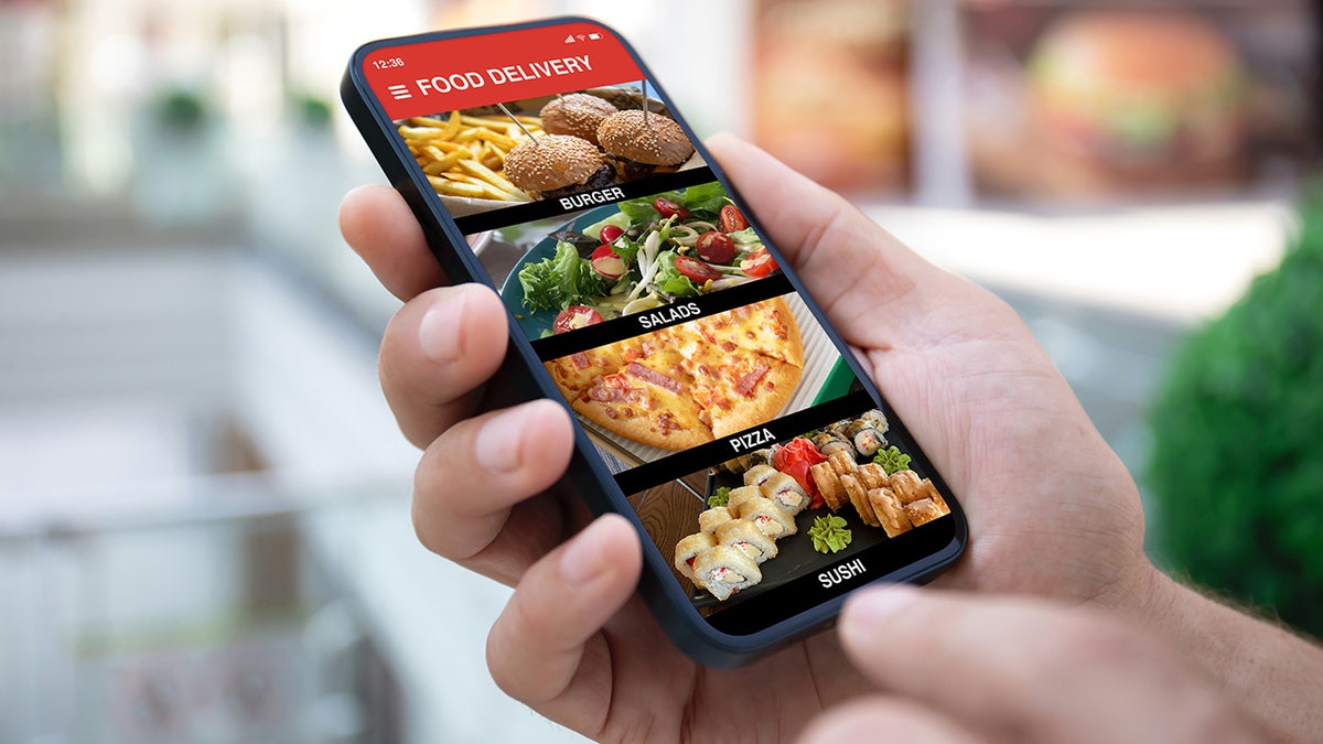 Variety of food delivery options seen on phone screen in person's hands, including pizza, burgers, salad and sushi.
