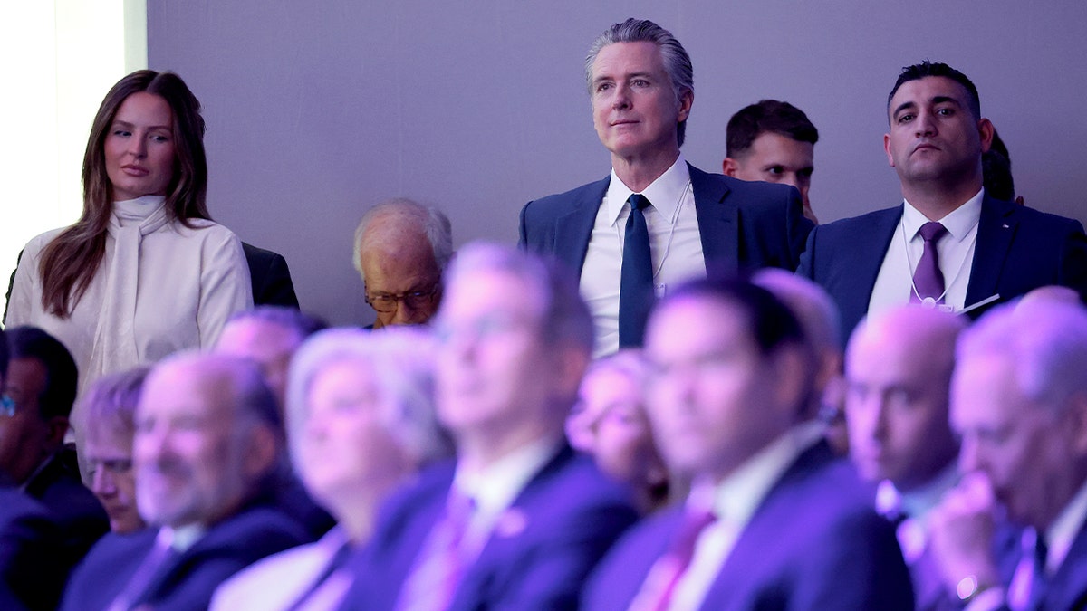 Gavin Newsom stands among attendees as he focuses on a speaker during a high-level international address.