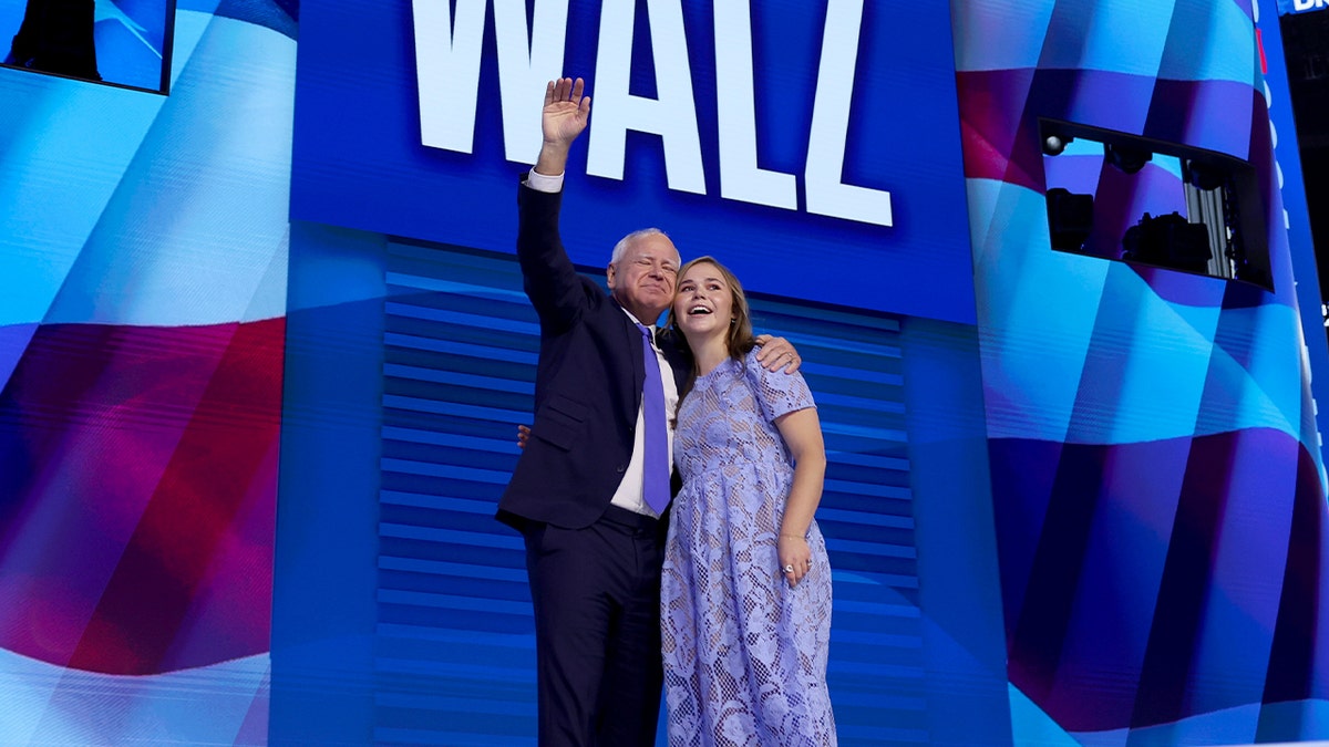 A Democratic nominee smiles and embraces his daughter amid cheering supporters on a convention stage.