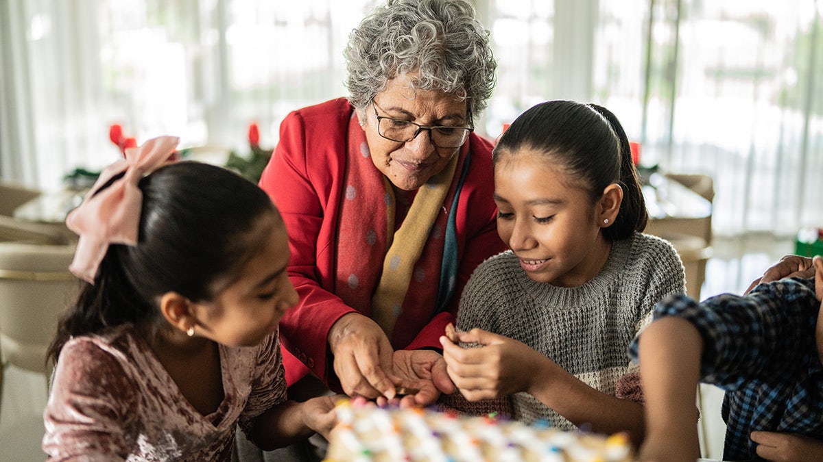 Grandma making gingerbread house with granddaughters.