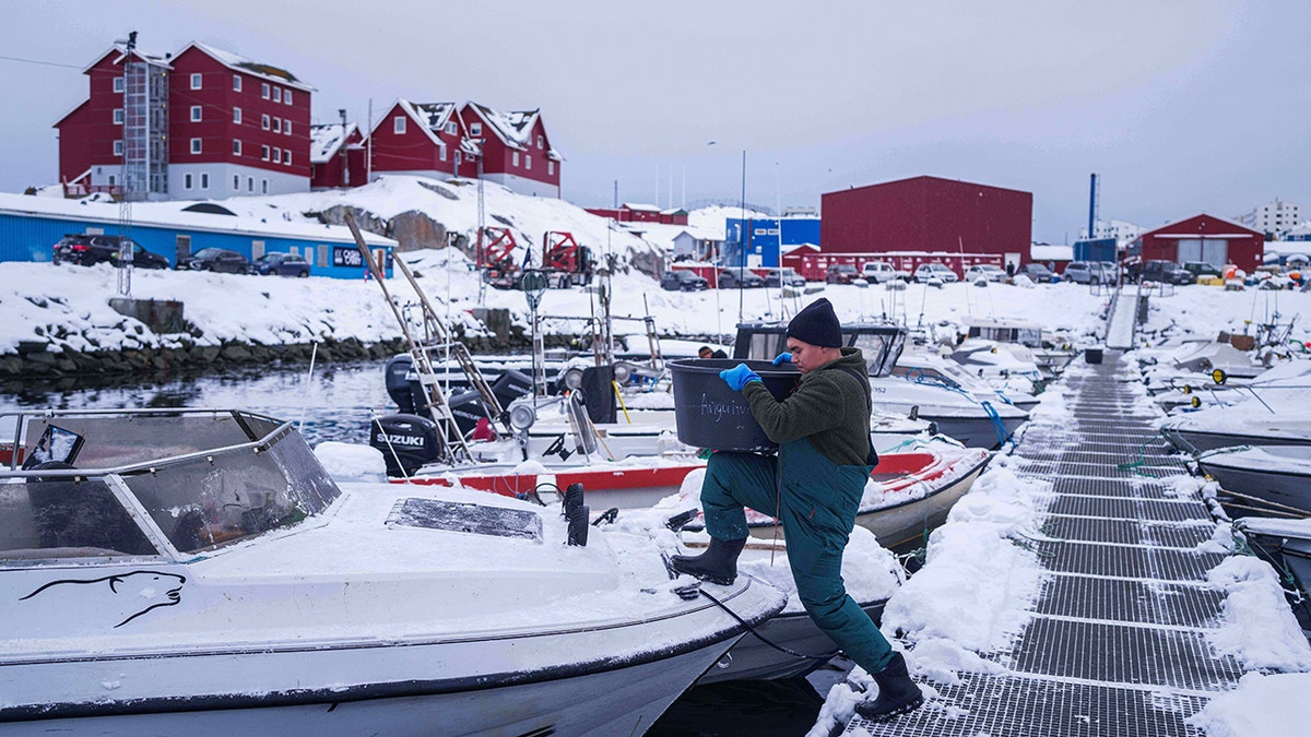 A fisherman carries a bucket onto a boat in Greenland