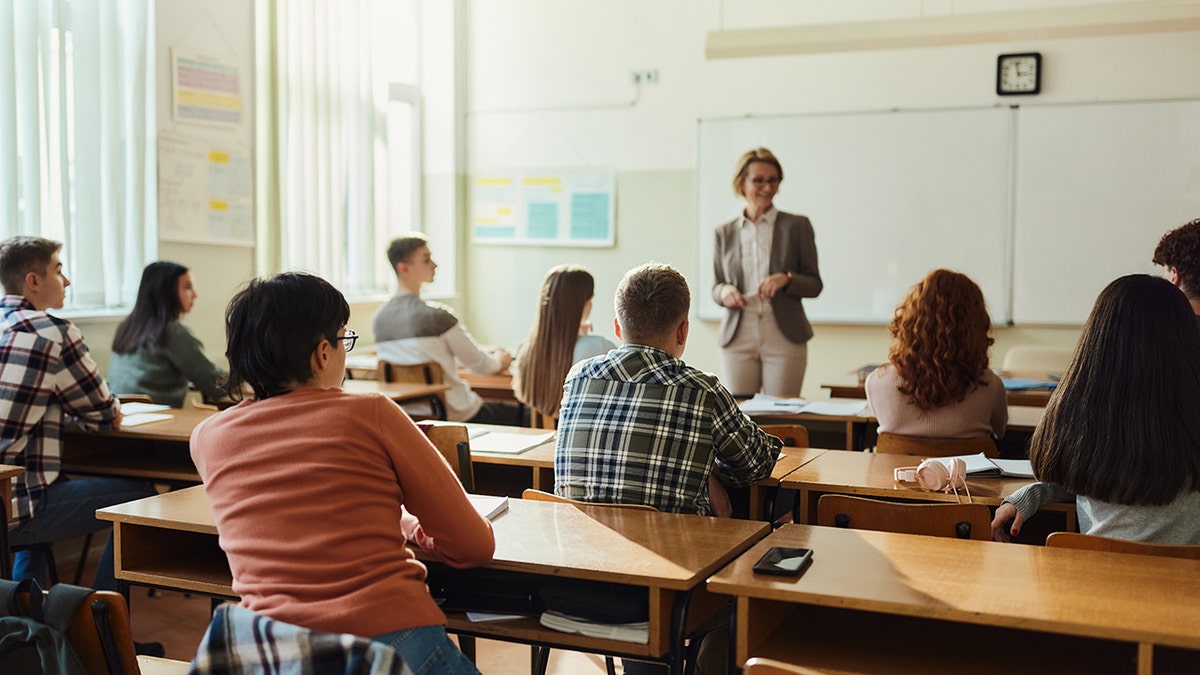 Boy in the middle listening to high school teacher in classroom