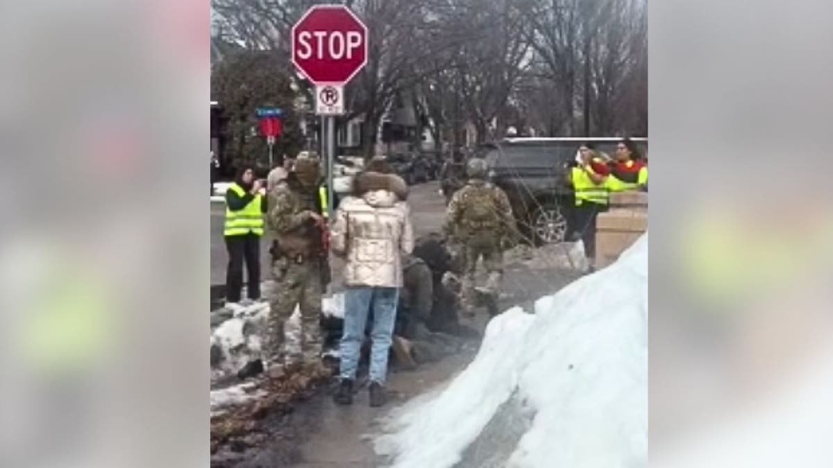 Federal agents stand over a person on the ground near a stop sign as others look on during an enforcement operation.