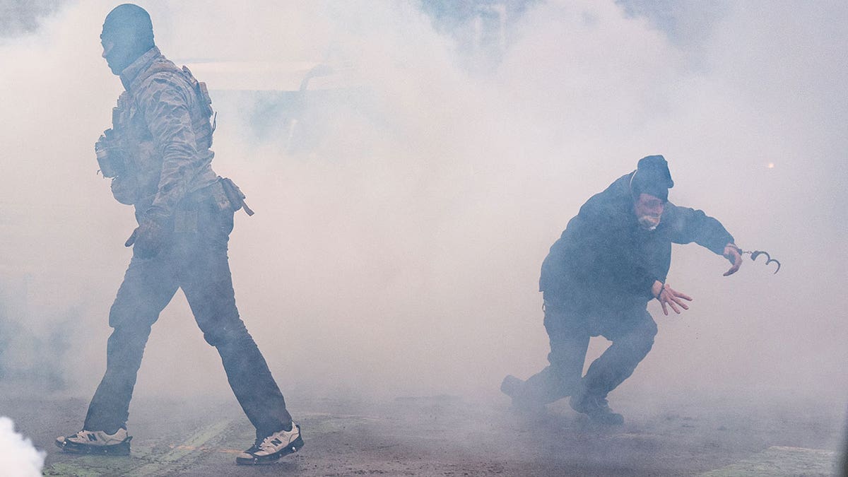 Un hombre esposado corriendo a través de una nube de gas lacrimógeno.