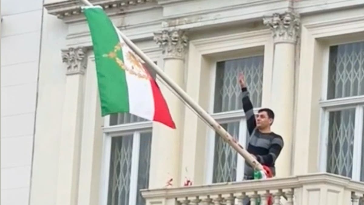 Protester stands on balcony of Iranian Embassy in London holding pre-1979 flag
