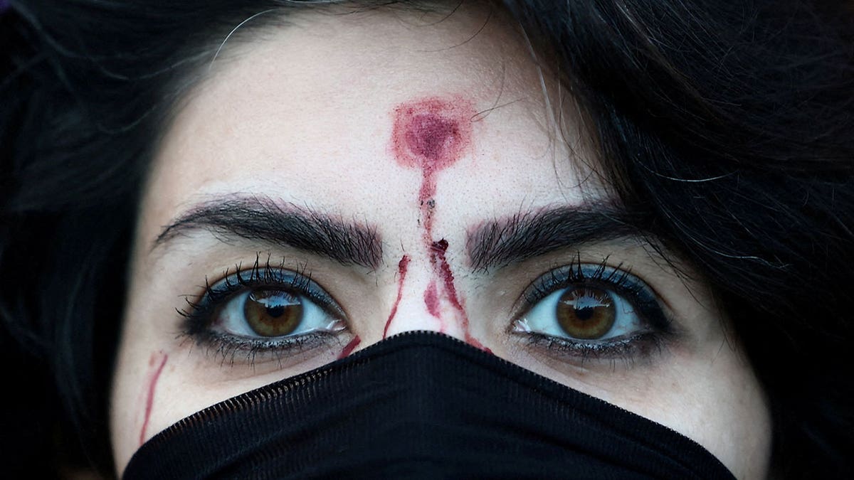 A woman with a mock-up of a gunshot bullet wound on her forehead looks on during a rally in Rome