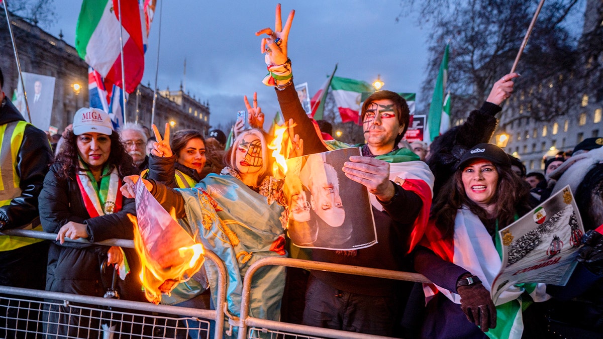 Protesters set fire to printed portraits during a demonstration on a central London street, with Iranian flags and placards visible nearby.