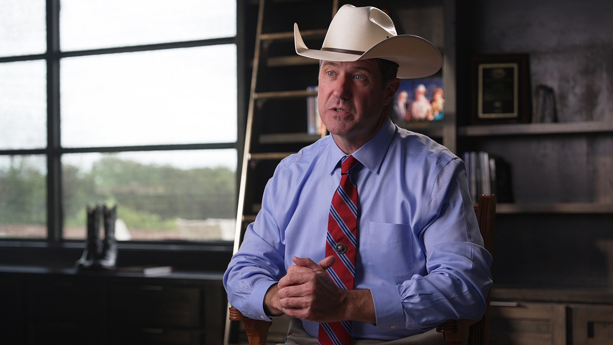 Texas Jim Holland con su sombrero de vaquero y botas de vaquero al fondo.