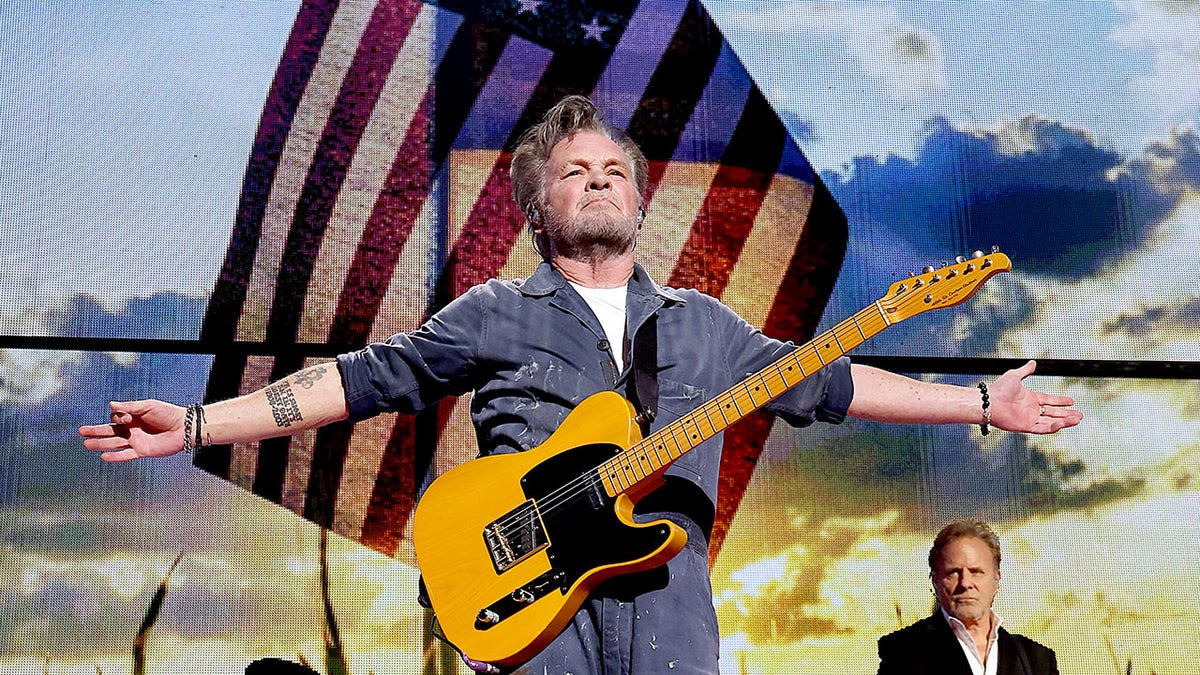 John Mellencamp si esibisce nel 2023 davanti alla bandiera americana