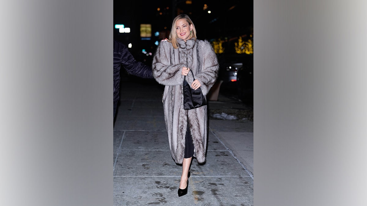 Kate Hudson walks on a New York City sidewalk wearing a long gray fur coat, black dress and pointed heels during a December 2025 outing.