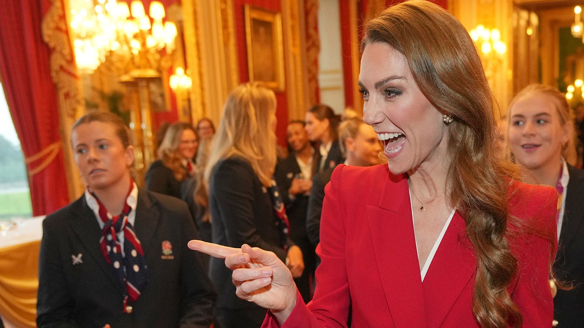 Kate Middleton in a red suit laughing and pointing.