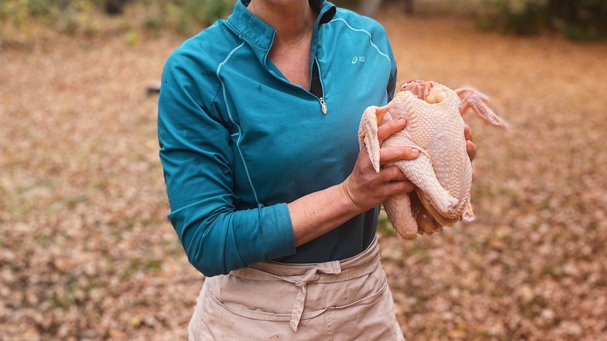 Katie Krejci holding a raw whole chicken outdoors, preparing poultry for cooking or processing.