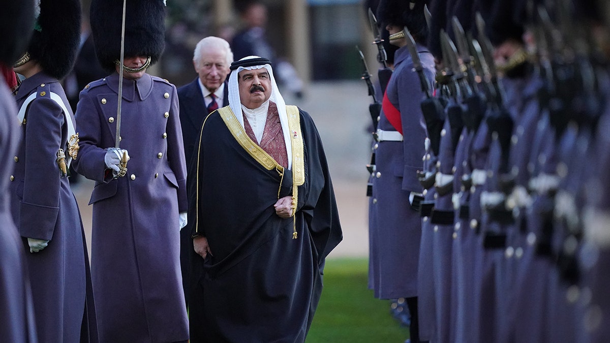 King Charles walking behind the King of Bahrain while observing the U.K. guards in uniform.