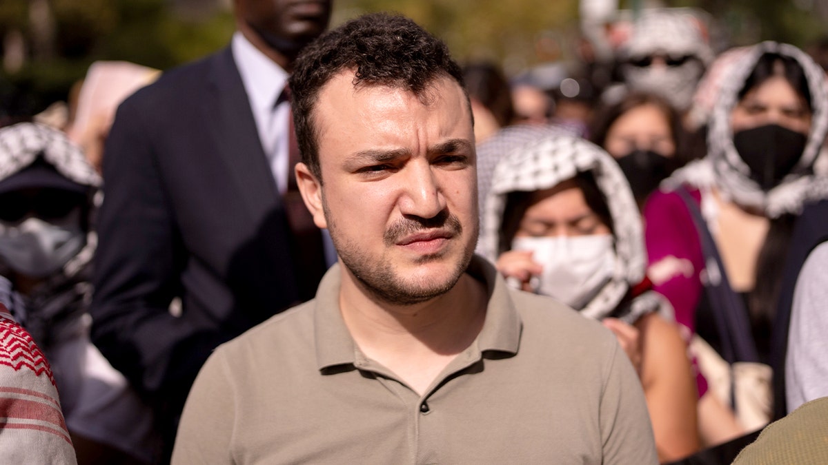 A man stands among demonstrators during an evening vigil near a university campus.