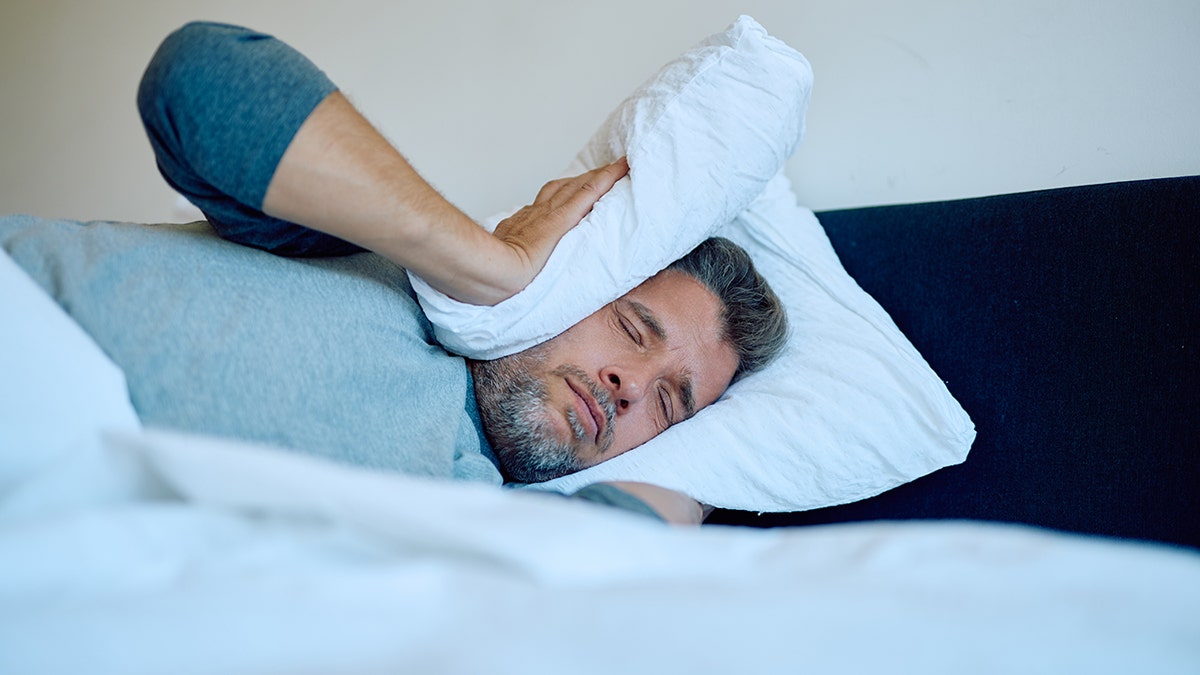 Man sleeping with a pillow pressed over his ear to block out noise.