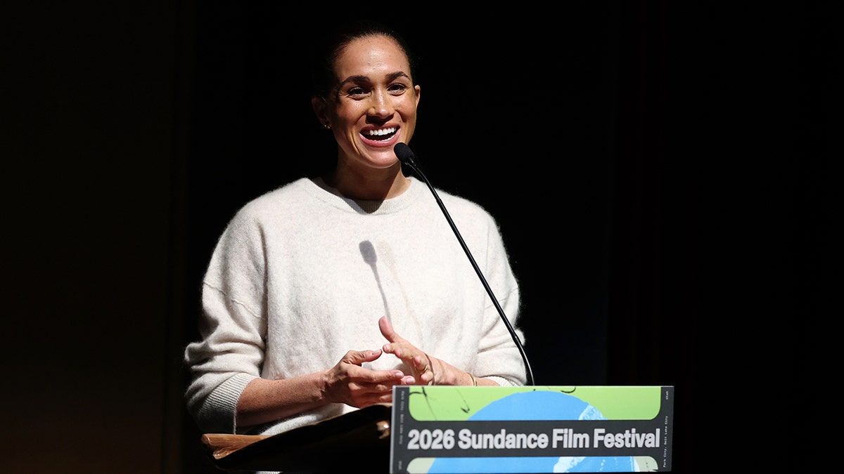 Meghan , vestida de blanco, hablando en un podio y sonriendo en el Festival de Cine de Sundance.