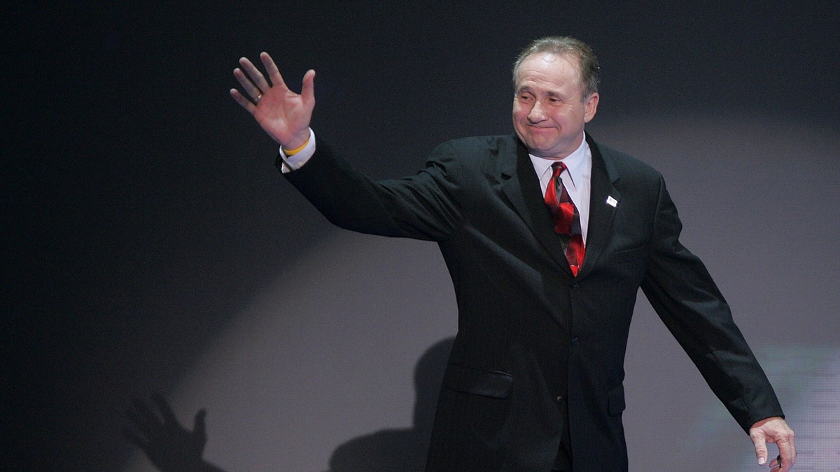 Michael Reagan walks onto a stage and waves