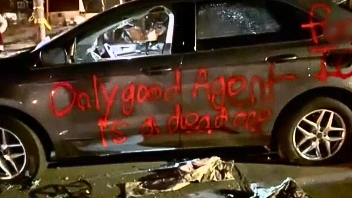 A damaged vehicle with red spray-painted graffiti reading 