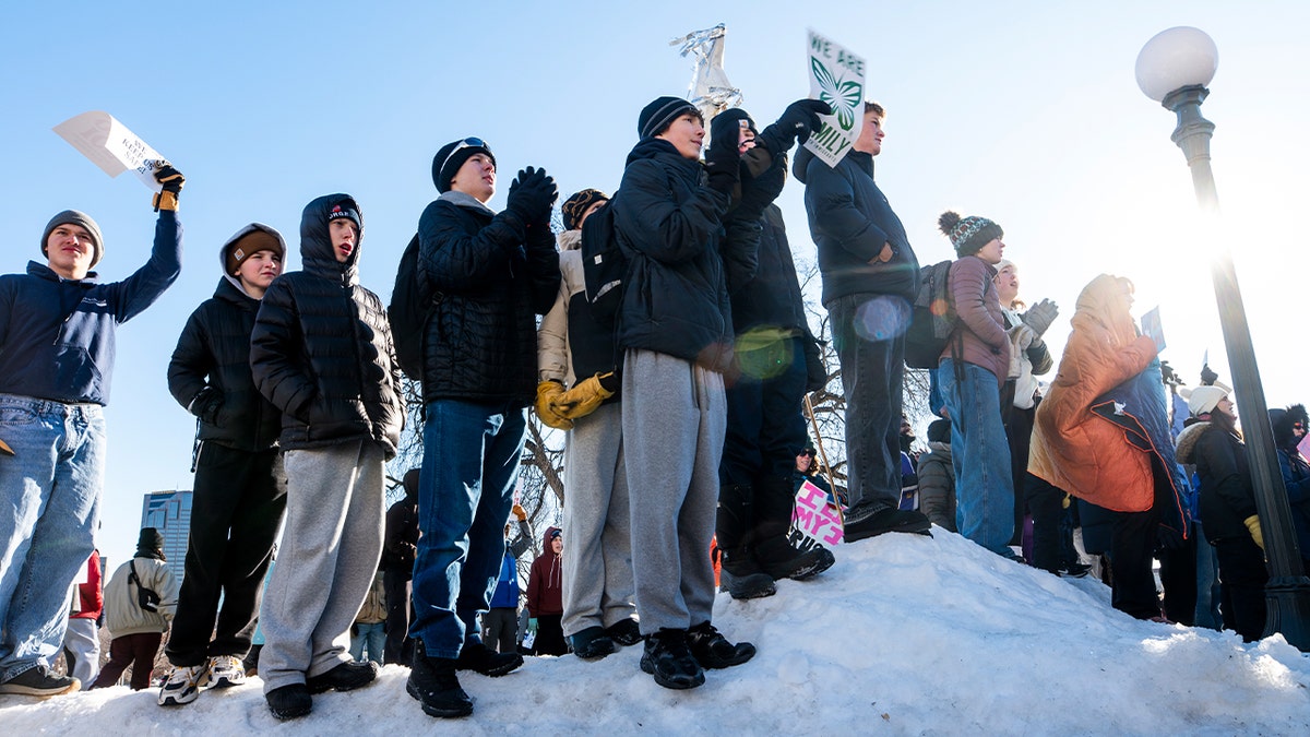 Students stand outside a government building holding signs during a daytime demonstration.