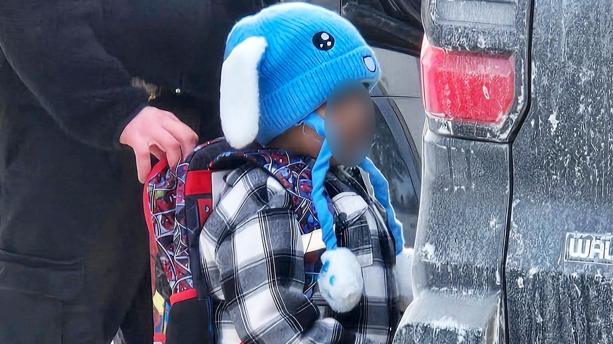 Niño con mochila de pie junto al vehículo.