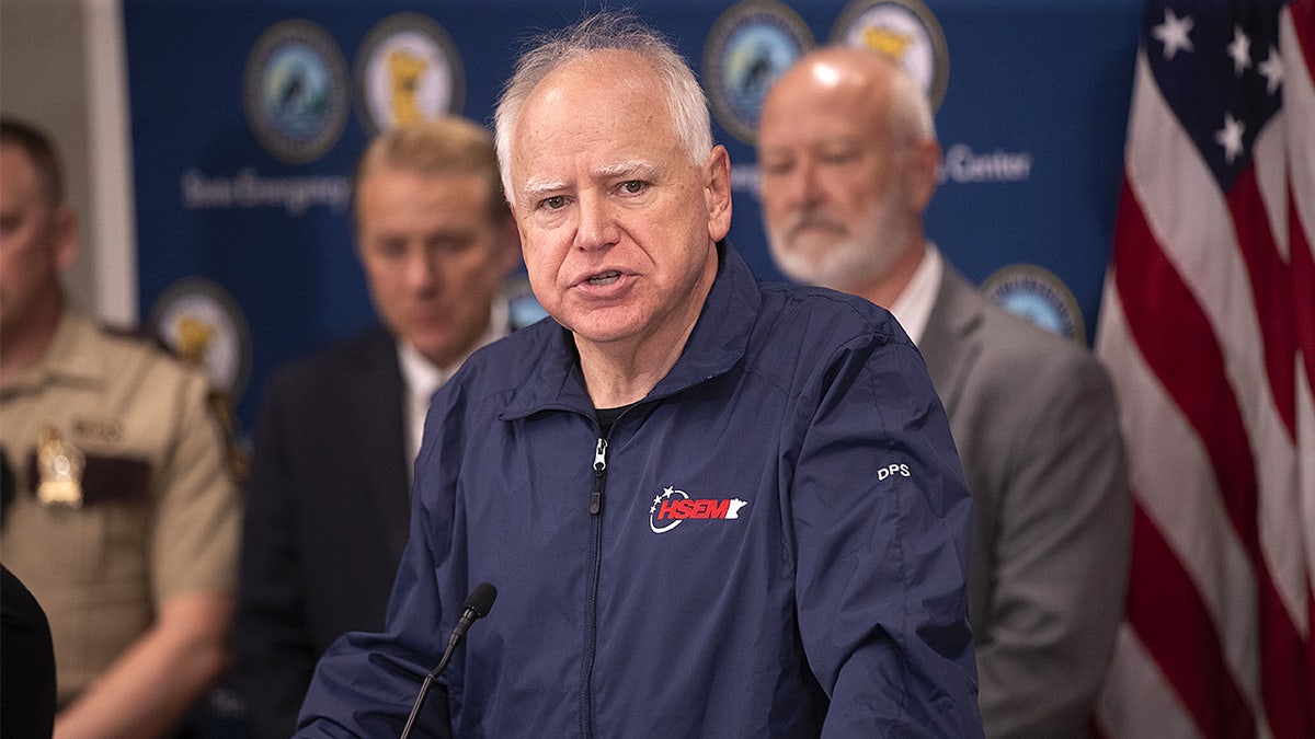 Minnesota Gov. Tim Walz speaks at a podium during a press conference inside an emergency management center.