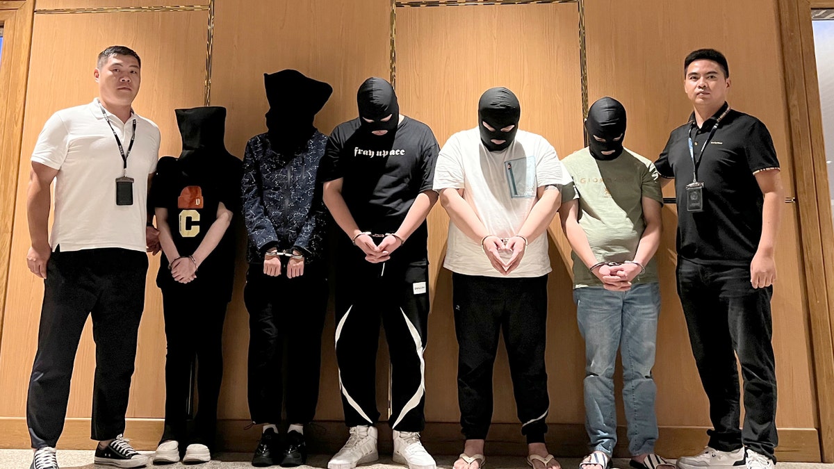 Agentes de policía escoltan a hombres detenidos durante un traslado bajo custodia en un aeropuerto.