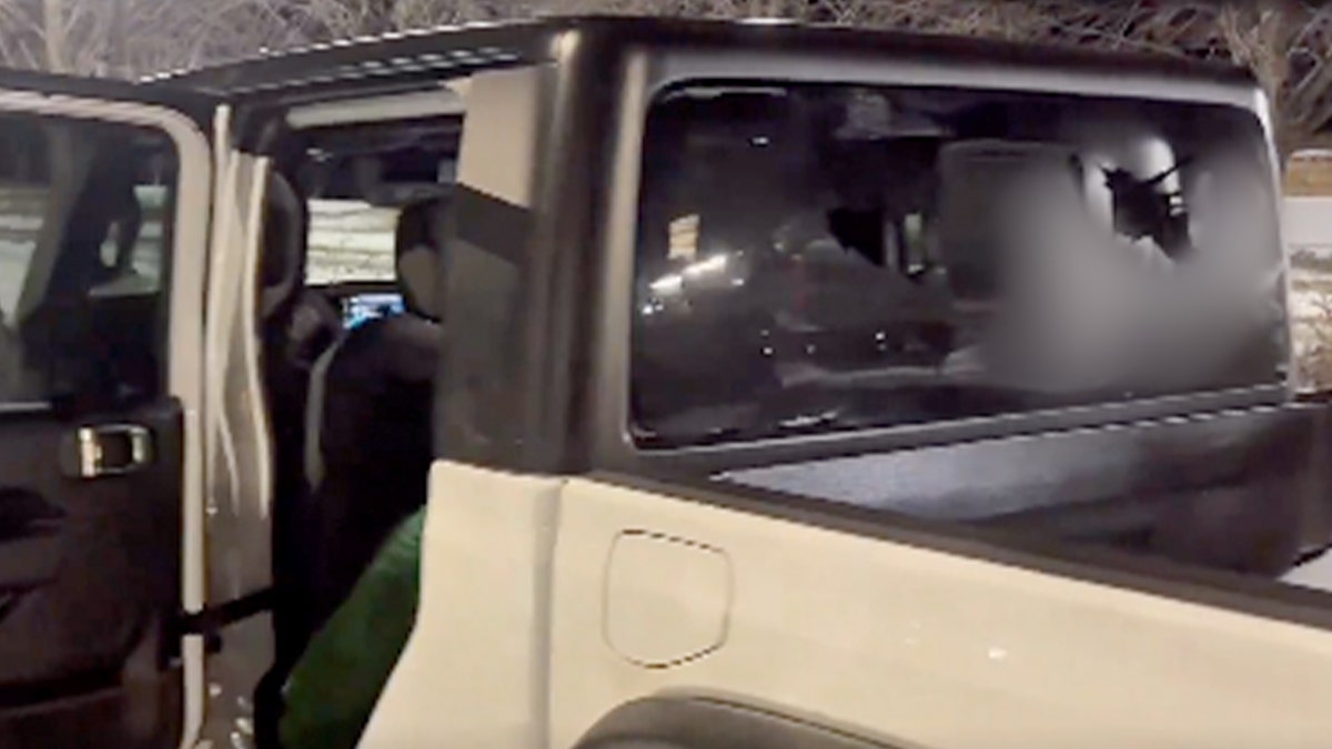 A truck with its rear door open is parked at night, with visible damage to the rear window after a confrontation near a protest.