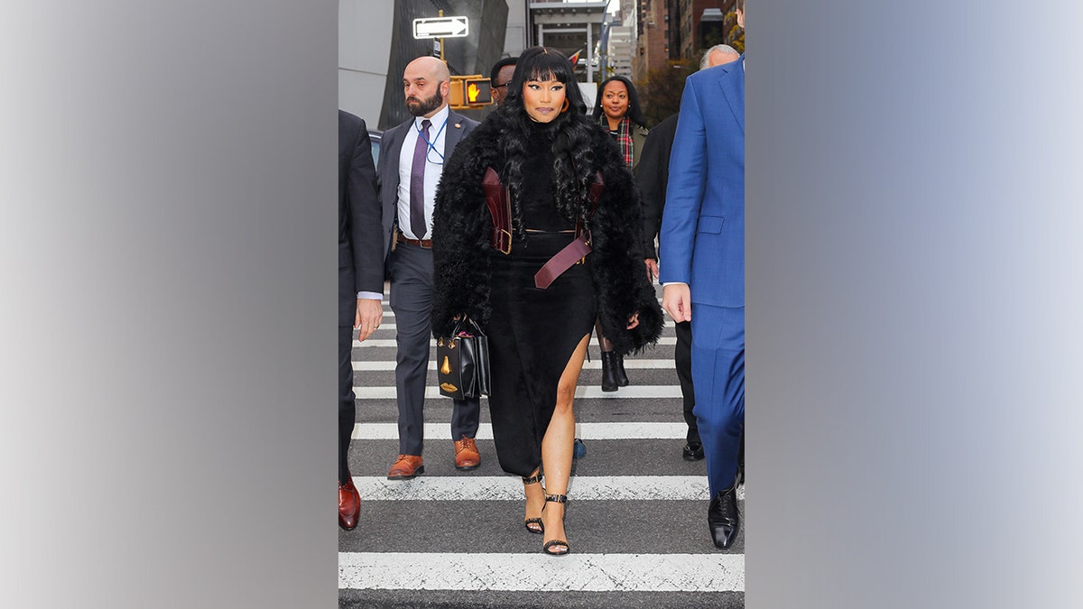 Nicki Minaj walks across a New York City street wearing a black fur coat and black dress during a November 2025 appearance.