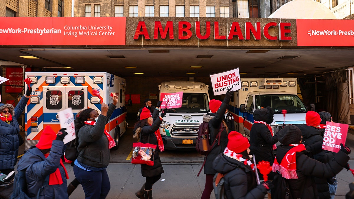 protesters dressed in red colors walk pass ambulance vehicles parked at a hospital during a strike
