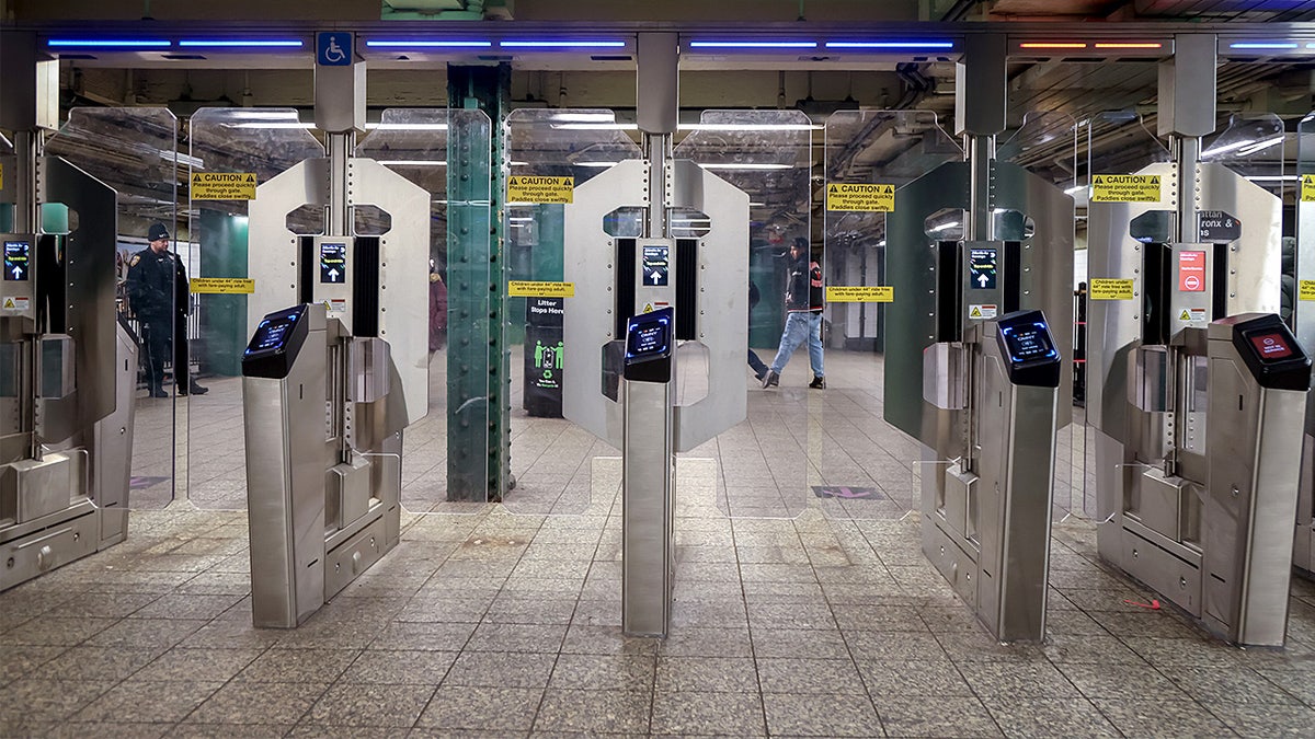 Subway turnstiles fitted with contactless payment readers are lined up inside a station entrance.
