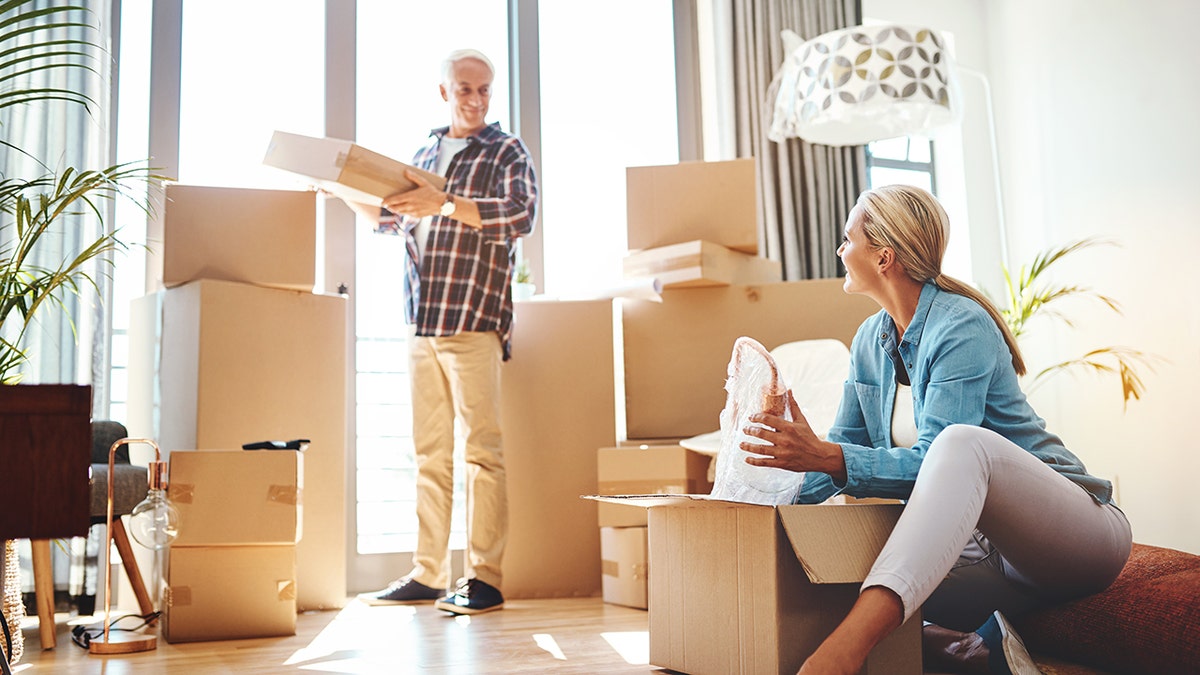 Older couple unpacking moving boxes together in a bright, modern living room.