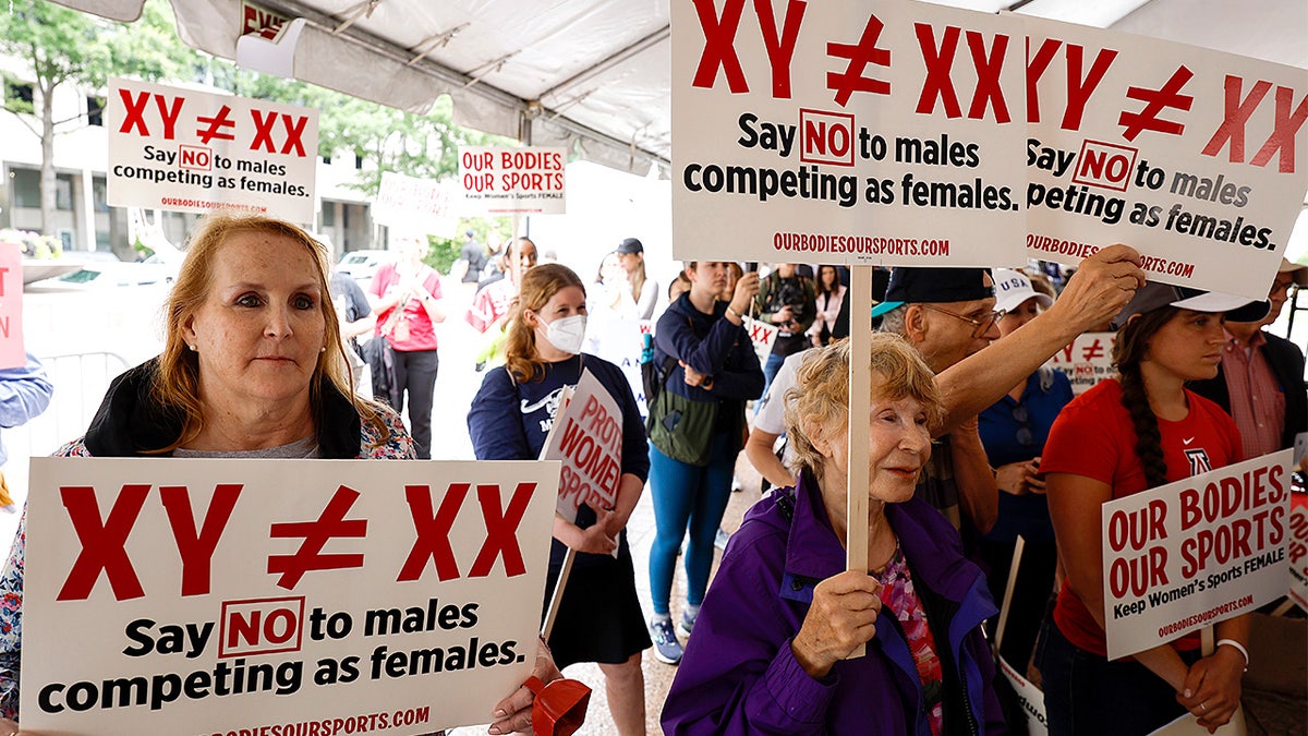 Demonstrators stand and listen to speakers during a rally advocating for women’s sports.