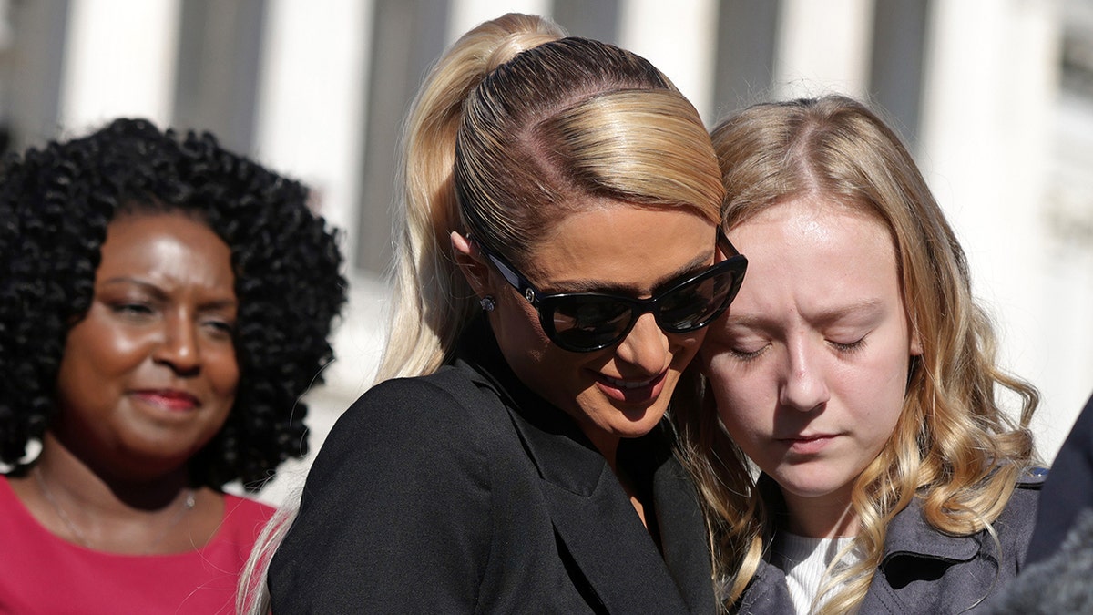 Paris Hilton embracing a young woman with her eyes closed.