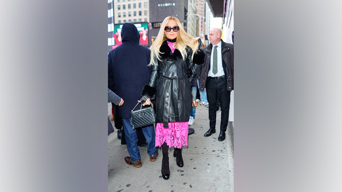 Paris Hilton in New York wearing a black leather coat with fur collar and cuffs, pink lace dress, and black handbag.