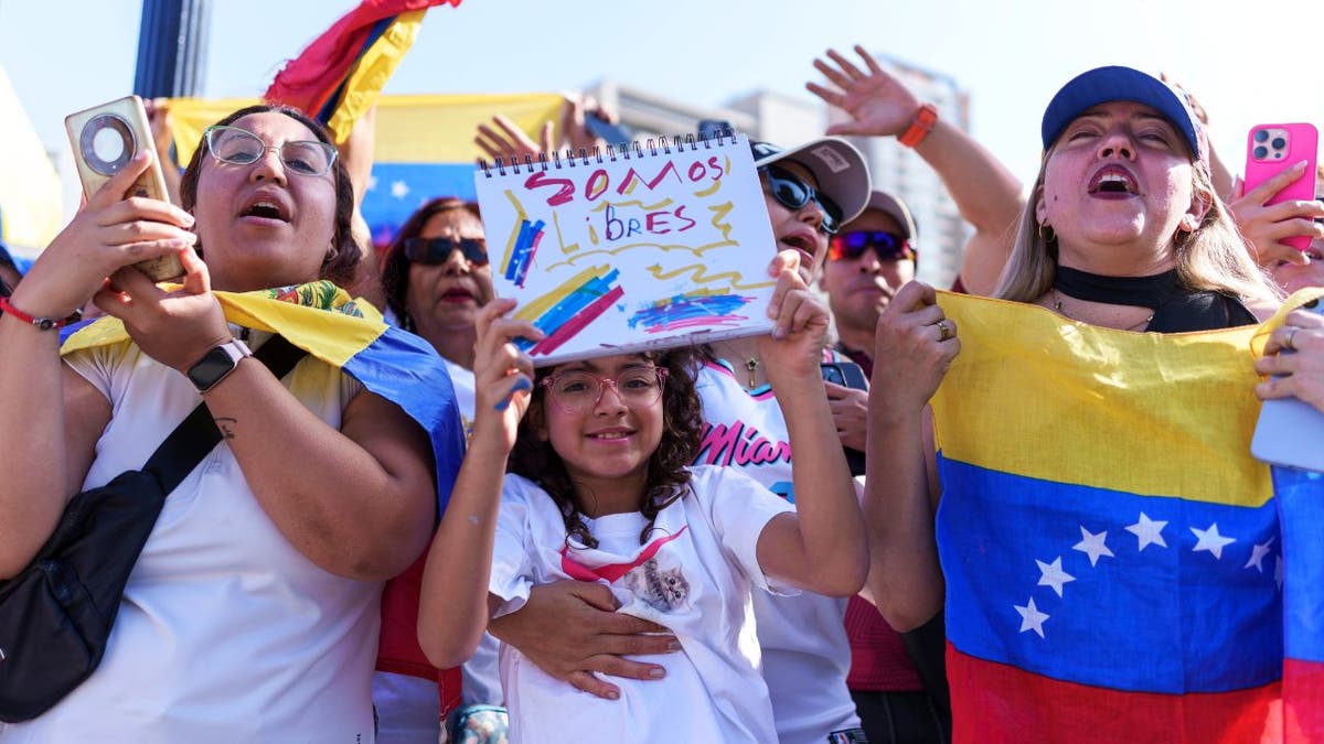 A child and adults in Santiago, Chile, wave Venezuelan flags and hold signs celebrating news of Nicolás Maduro’s capture.
