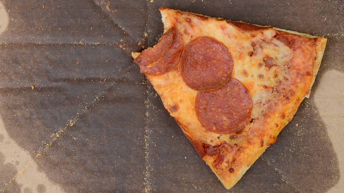 Single cold slive of pepperoni pizza left behind with one bite taken out in greasy box.