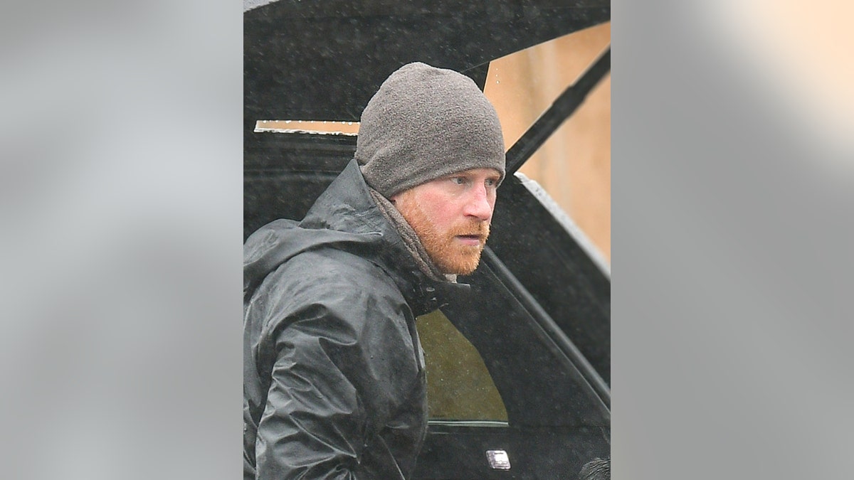 El príncipe Harry una chaqueta gris y un gorro a juego, posa serio delante de un coche en Montecito.
