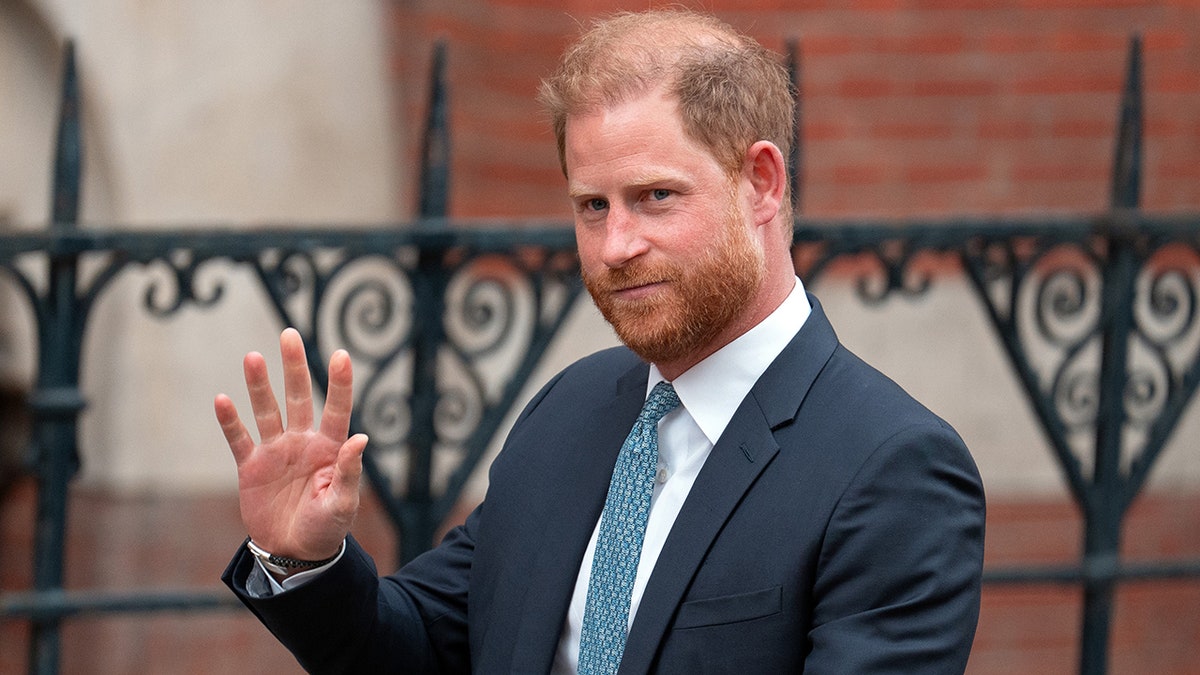 Prince Harry waving in a dark blue suit.
