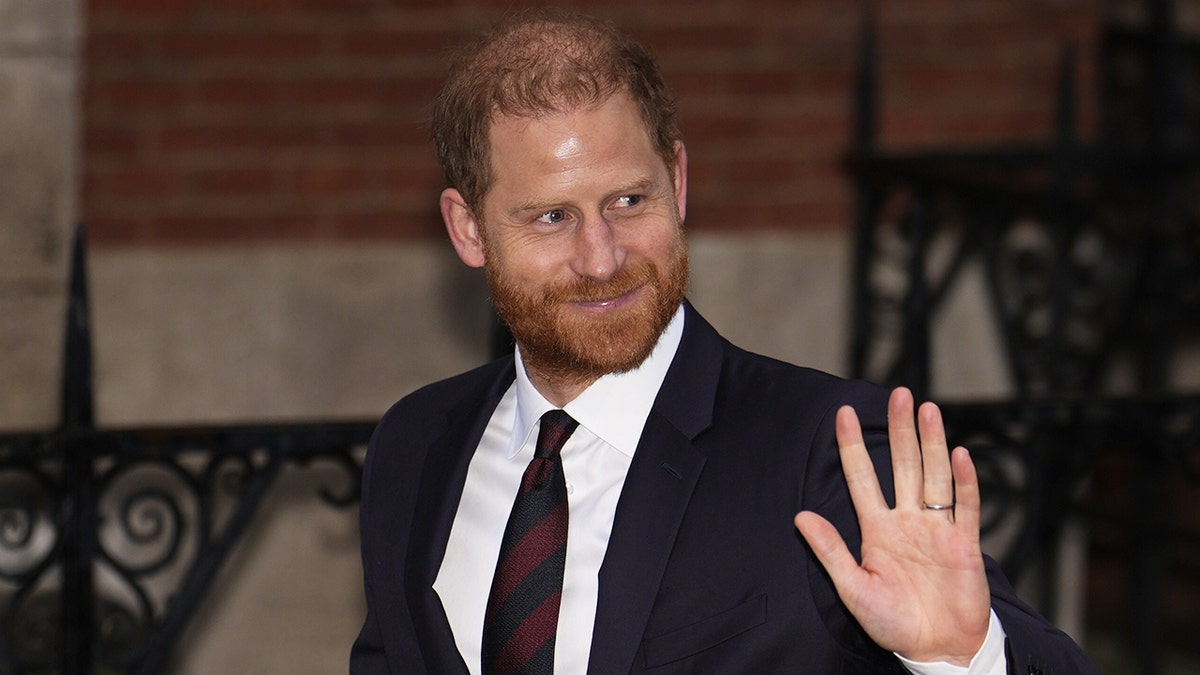 Prince Harry waving in a dark suit after leaving the courtroom.